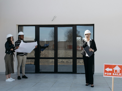 Agents viewing house plans with "for sale" sign outside property.