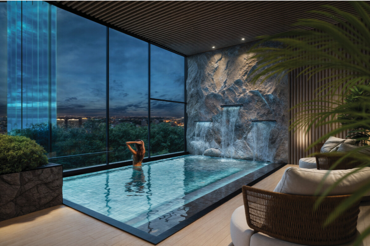 "Luxury indoor swimming pool at Montbleu Westlands with waterfall feature, floor-to-ceiling windows, city skyline views, lounge seating, and modern spa design"